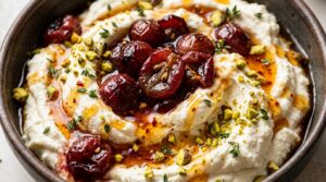 Ultra close-up macro of whipped ricotta dip topped with roasted caramelized red grapes, hot honey drizzle, and chopped pistachios